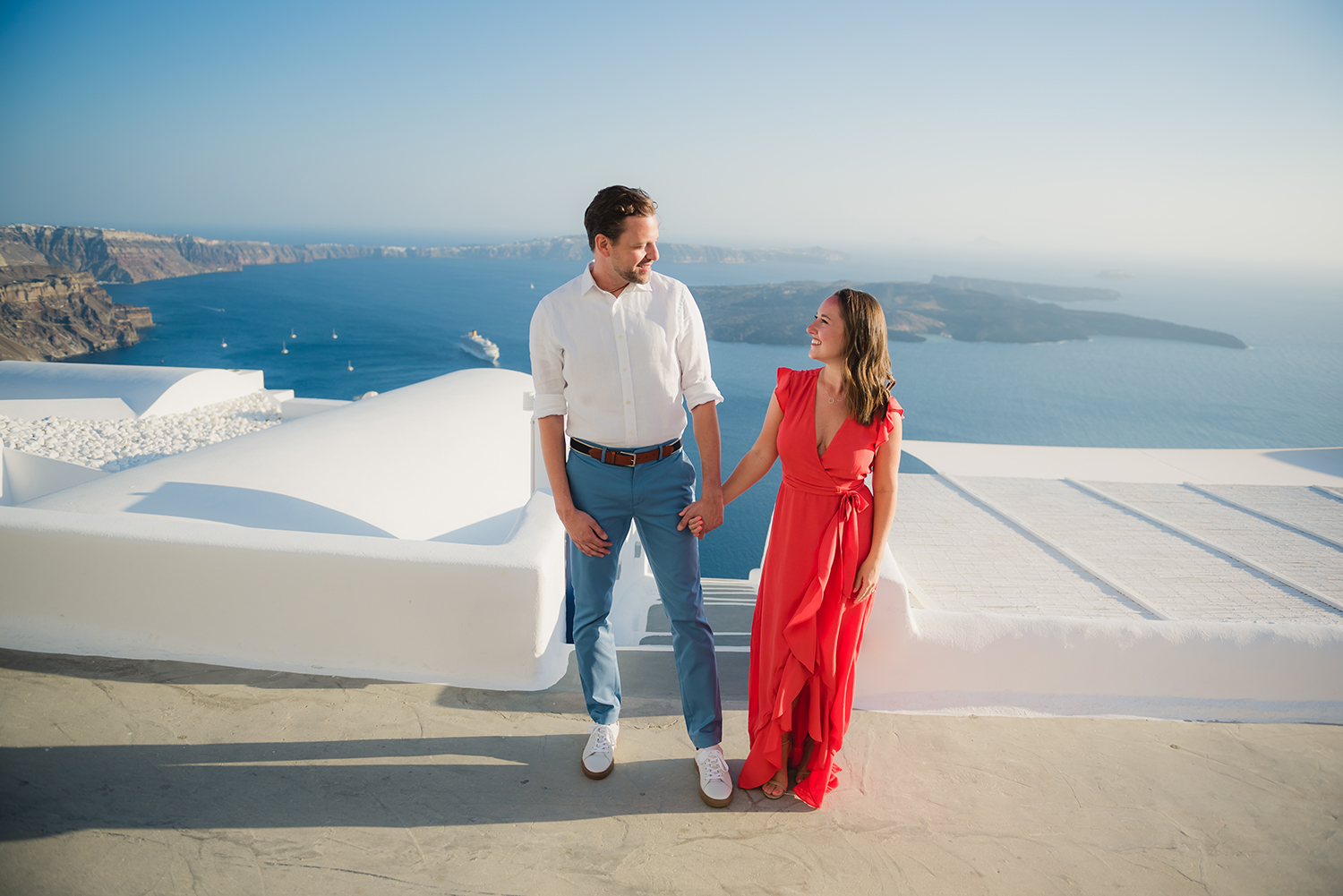 Couple holding hands by the Santorini view. Volcano , white washed houses and steps.