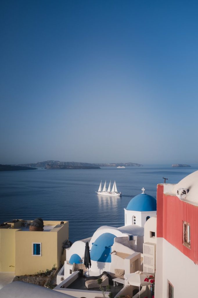 Sail boat in Santorini, passing by blue domed church in Aegean Sea. Oia village.