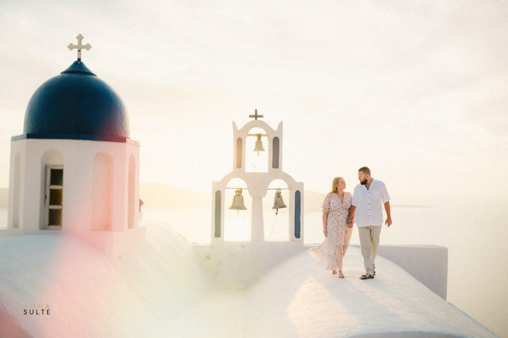 Couple walking on a rooftop with sunset in the background in Imerovigli, Santorini.