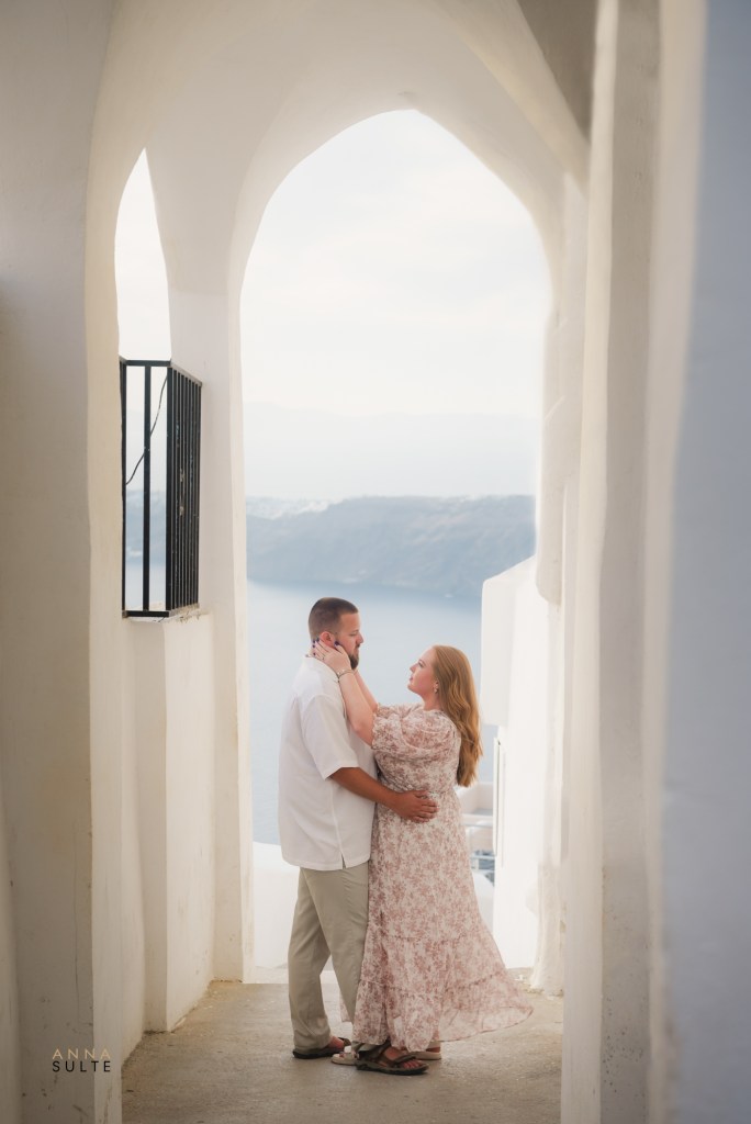 Couple hugging in a quiet alley in Imerovigli, Santorini, surrounded by whitewashed walls.
