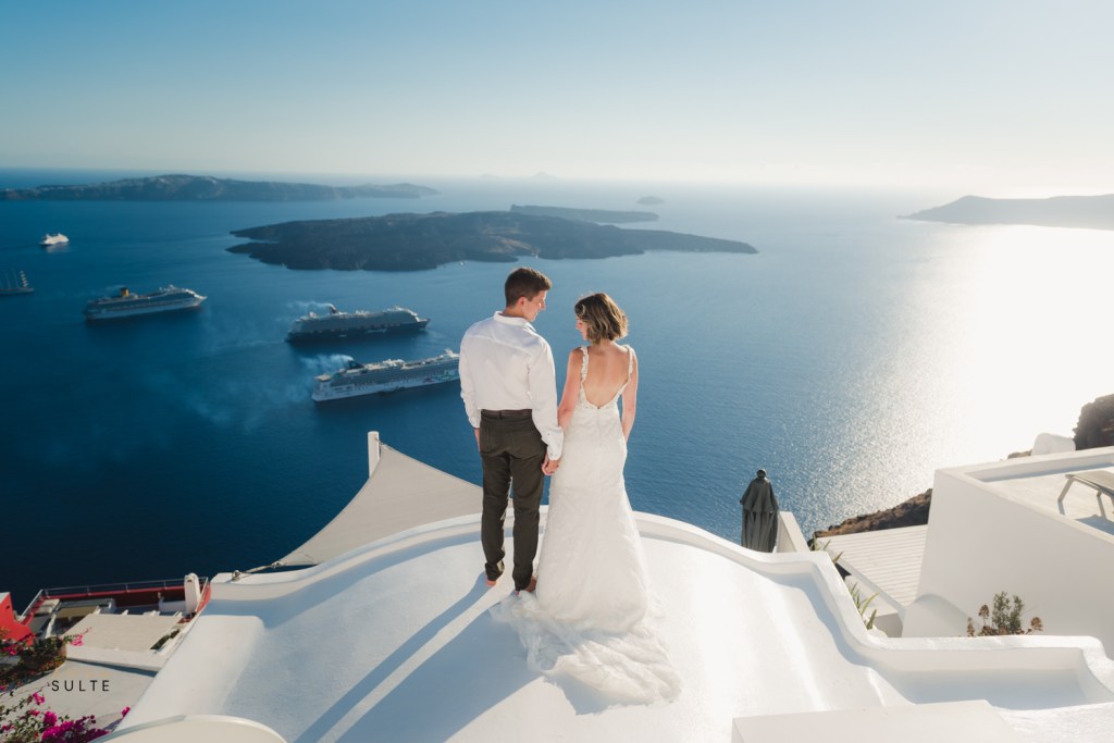 Couple holding hands on a rooftop overlooking a scenic view of Santorini.