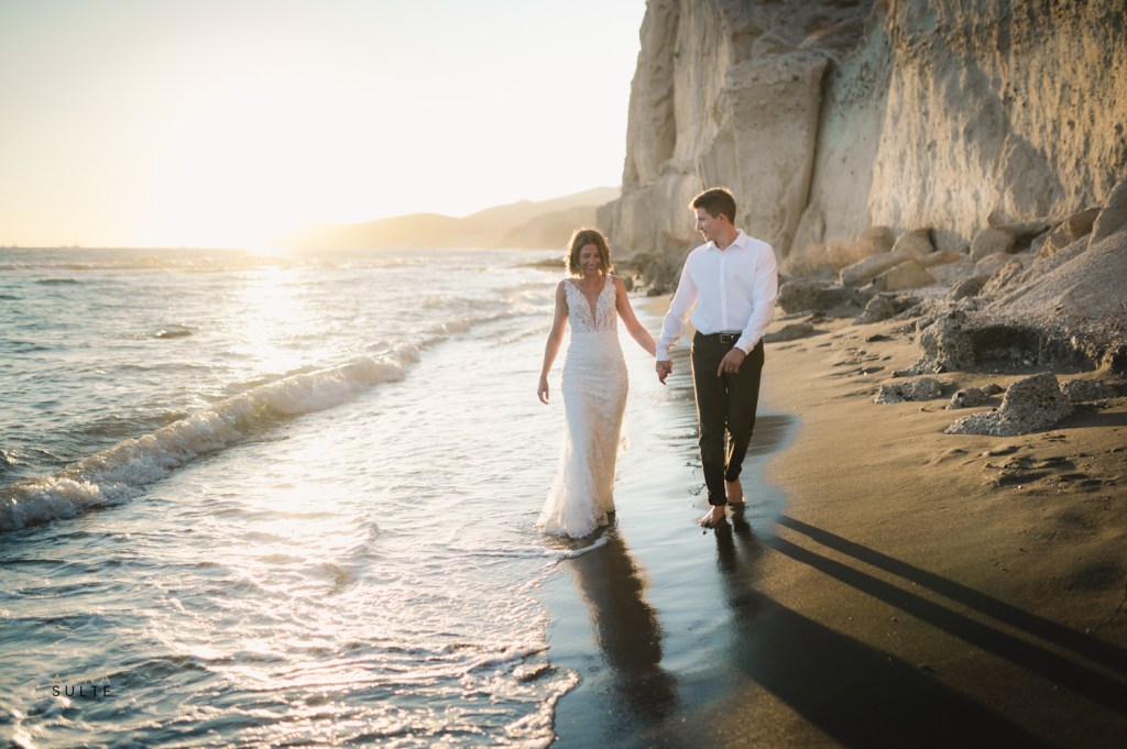 A wedding couple walking at the beach in Santorini. White cliffs behind them.