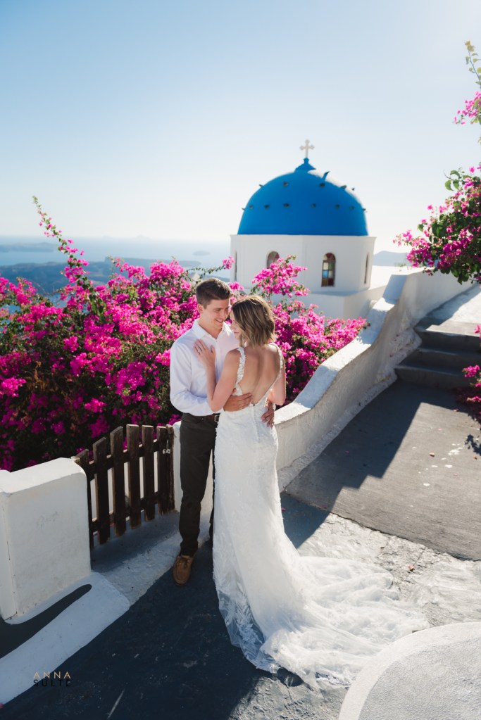 Santorini blue church, pink flowers and a couple hugging next to the church.