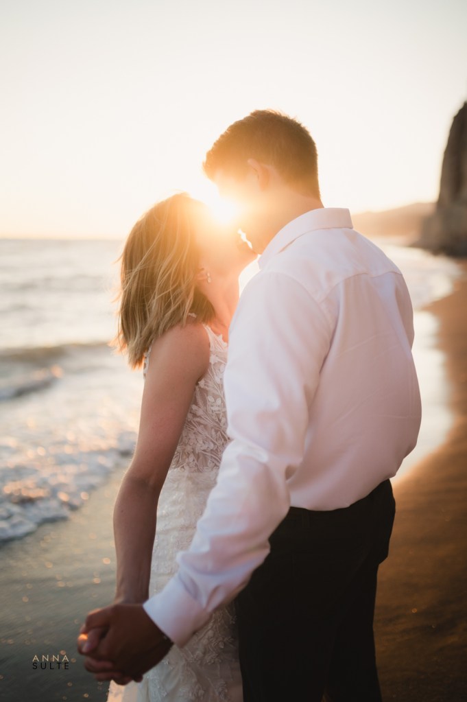 Couple hugging on a sandy beach in Santorini, with striking white cliffs in the background.
