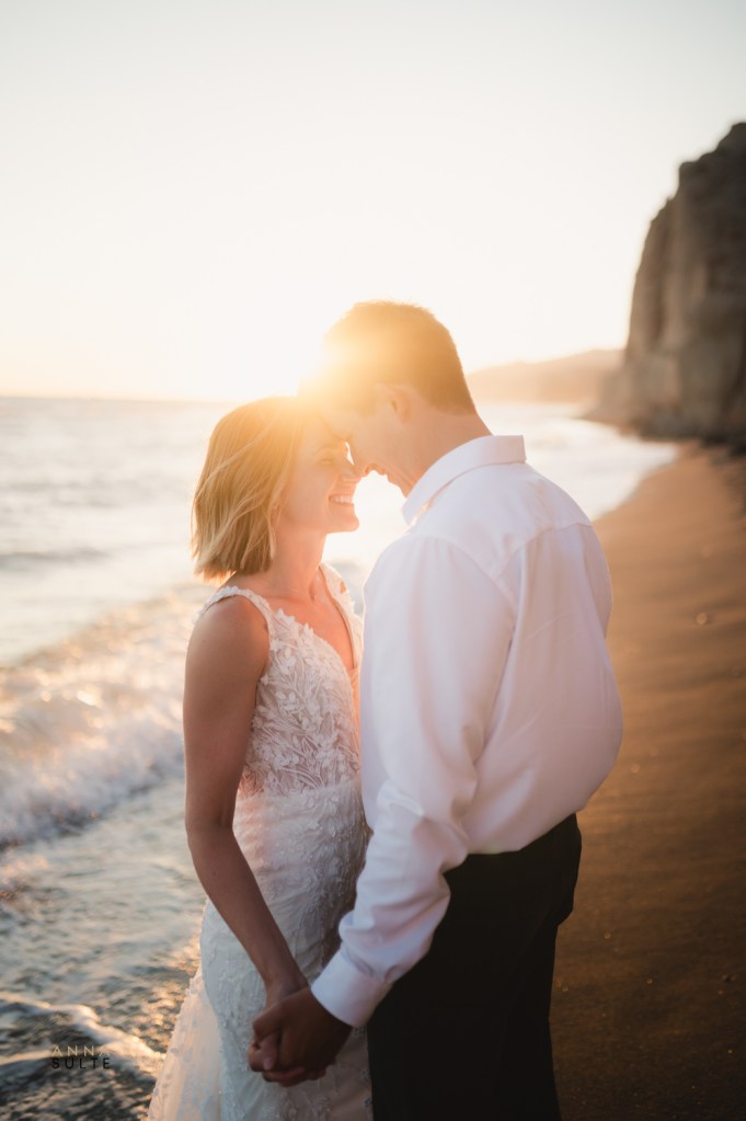 Couple hugging on a sandy beach in Santorini, with striking white cliffs in the background.