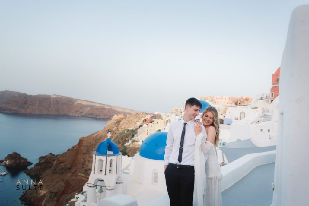 Couple posing in front of Santorini’s iconic blue domes with the Aegean Sea in the background.