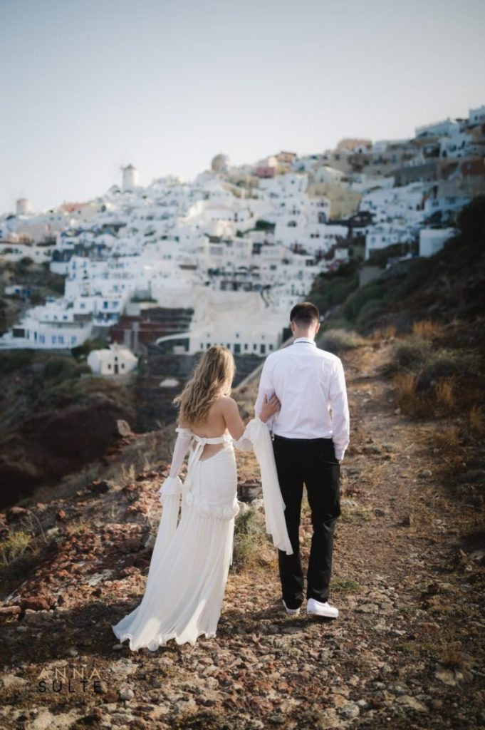 Couple walking hand-in-hand through the charming white alleys of Oia, Santorini.