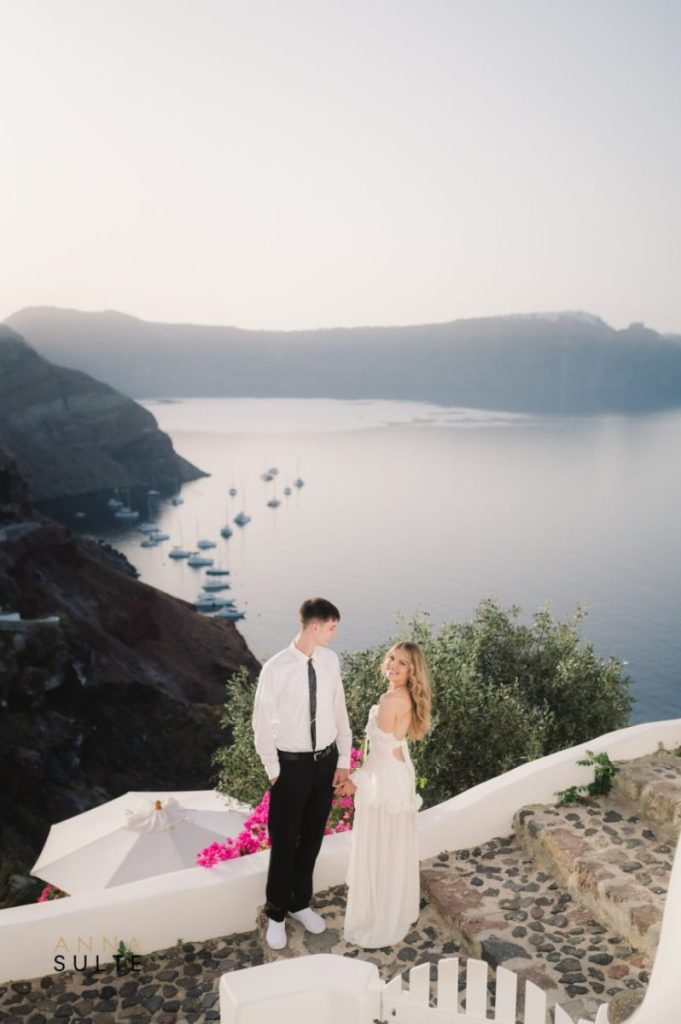 Couple standing hand in hand in the charming streets of Oia, surrounded by white buildings.
