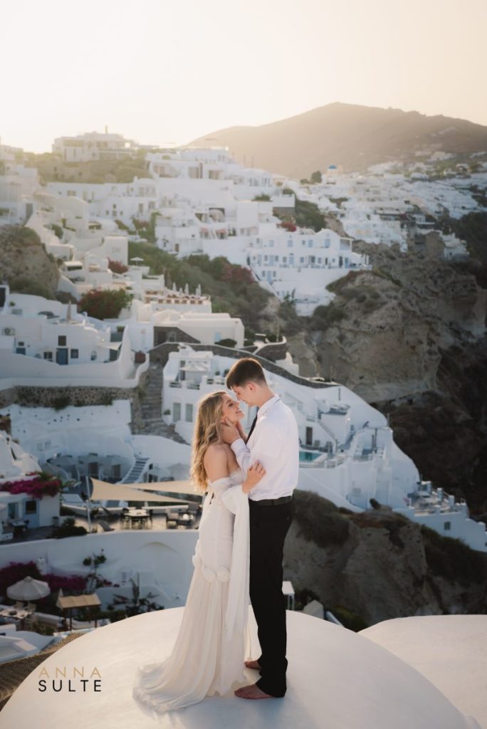 Couple embracing during a sunrise elopement in Santorini, with stunning cliffs in the background.