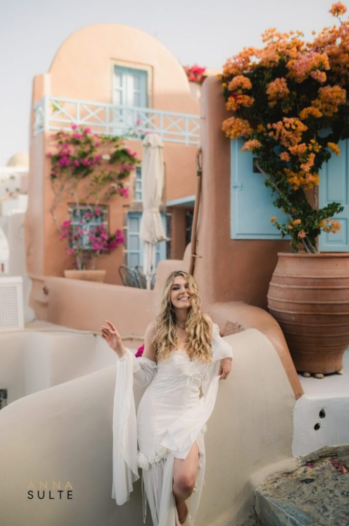 Woman in a flowy dress posing elegantly on a Santorini terrace overlooking the caldera.