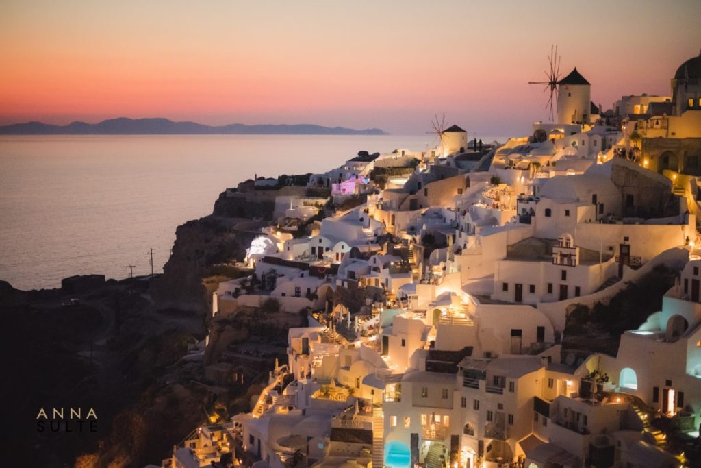 Sunset in Oia, Santorini. Windmills, city lights and blue hotel pools.