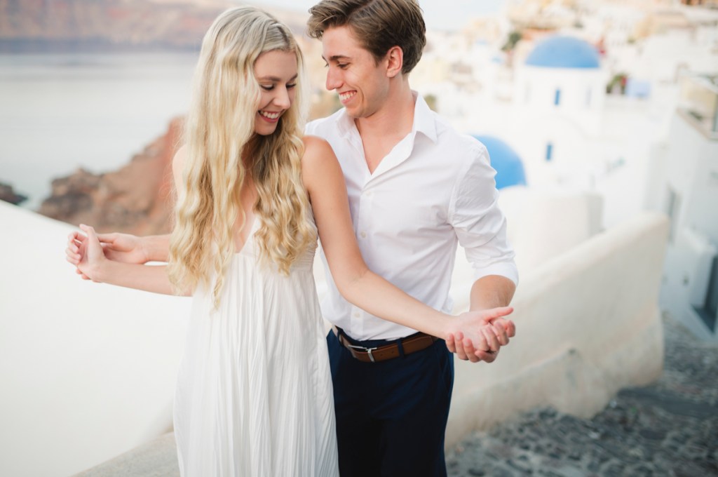 Couple in Oia with blue domes in a bacground.