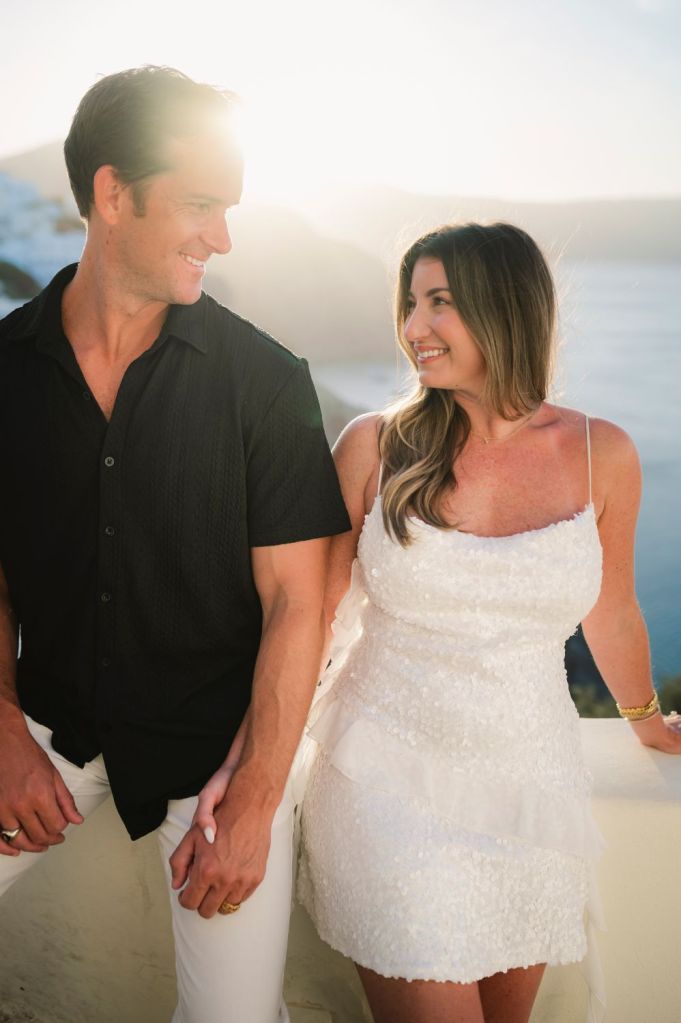Story-driven photography in Santorini, Greece, featuring a couple at sunrise sitting on a ledge in Oia.