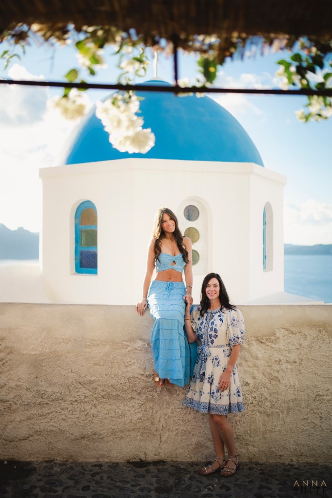 Teen girl with mother next to blue dome in Santorini, Greece.