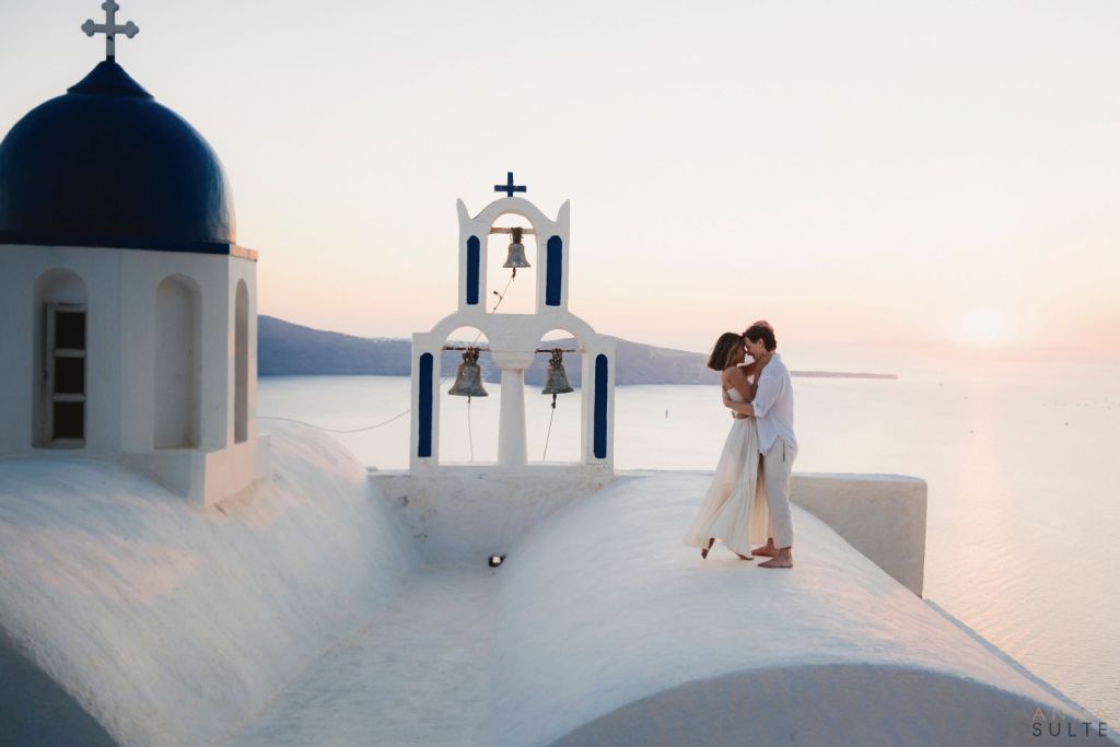 A couple sharing a quiet sunset moment in Imerovigli, with soft golden light, caldera views, and the peaceful evening atmosphere of Santorini.