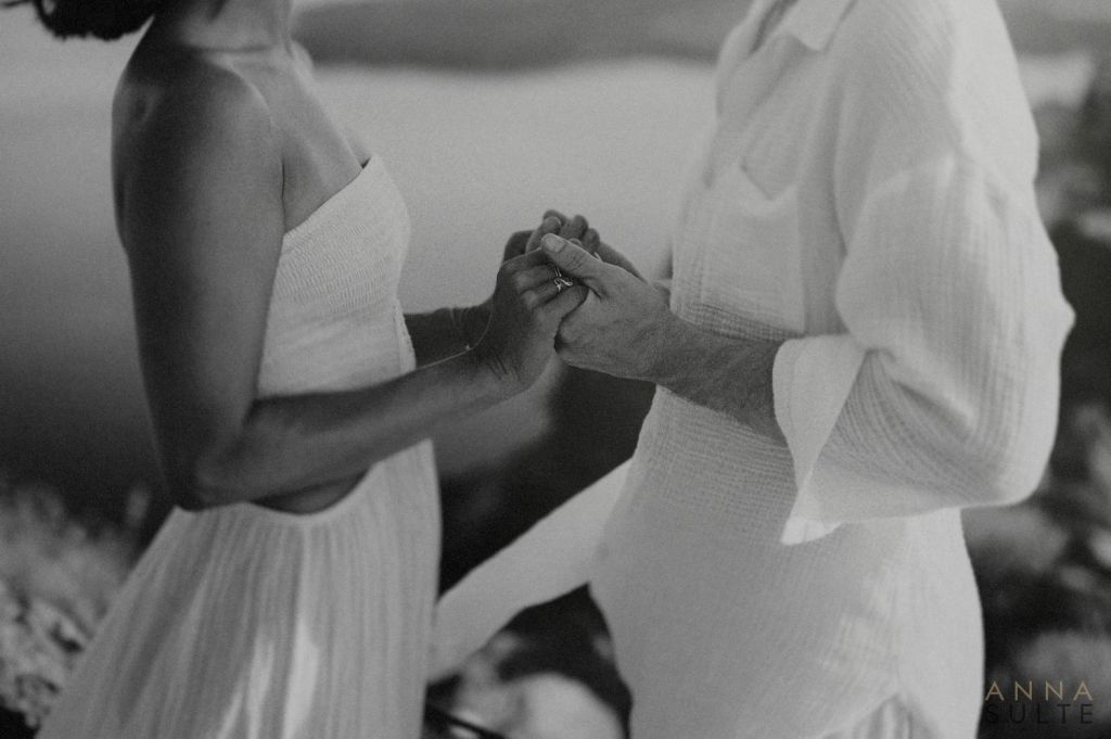An intimate Santorini couples photoshoot in Imerovigli at sunset. Couple holding hands. Surrounded by warm tones, open views, and a calm, romantic setting.