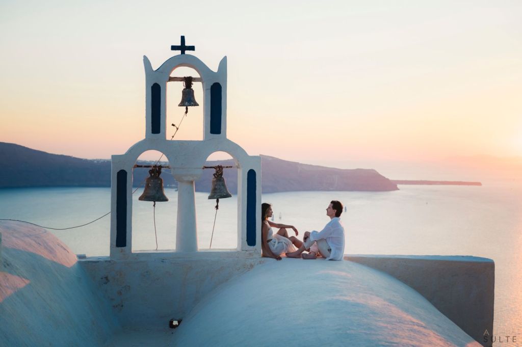 A couple enjoying an intimate sunset moment in Imerovigli, with sweeping caldera views, soft golden light, and the unique atmosphere of Santorini at dusk.