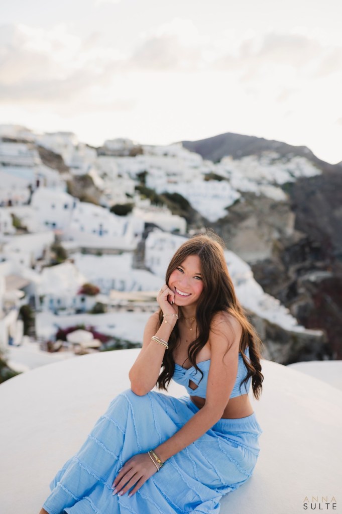 Teen girl sitting on rooftop terrace Santorini playful pose