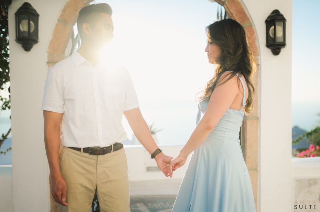 Couple holding hands on a whitewashed terrace in Firostefani, Santorini, capturing natural sunset light