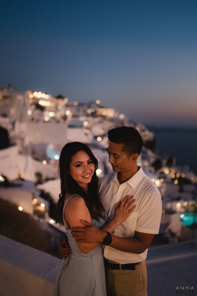 Romantic couple portrait at dusk with city lights of Santorini in the background, perfect for couples photoshoot.