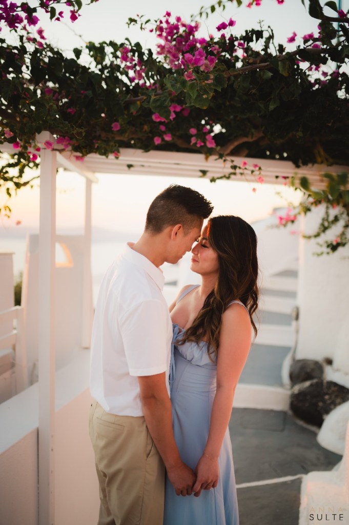 Engagement couple standing under bougainvillea archway in Firostefani, Santorini, during a natural light photoshoot.