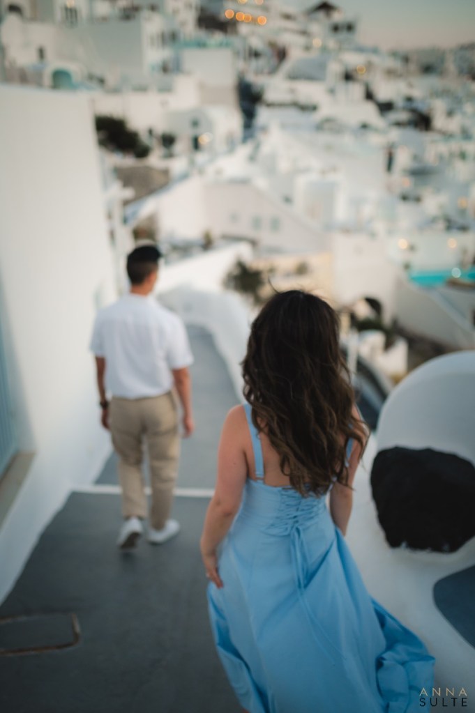 Woman walking ahead of her partner along a pathway at sunset, Santorini, perfect for couples photography.

